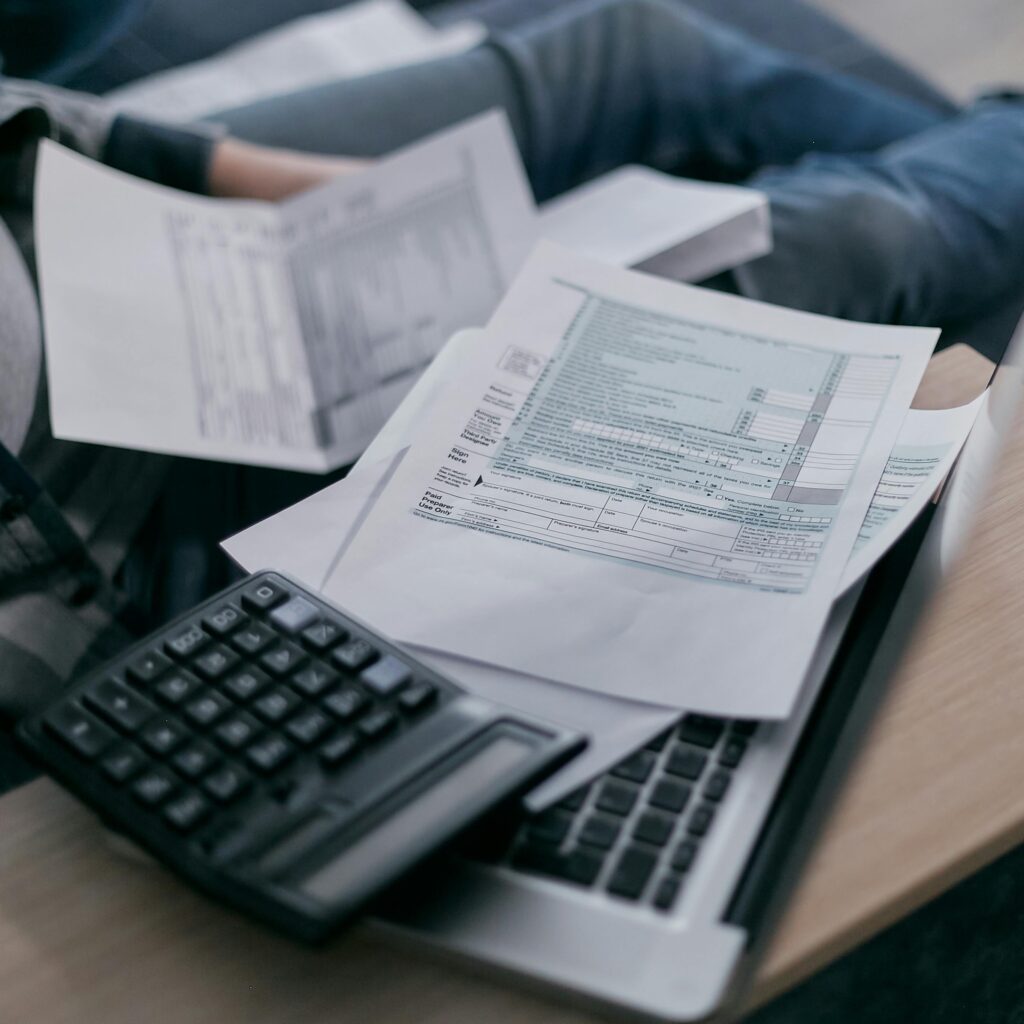 A close-up of tax forms, a calculator, and papers scattered on top of an open laptop.